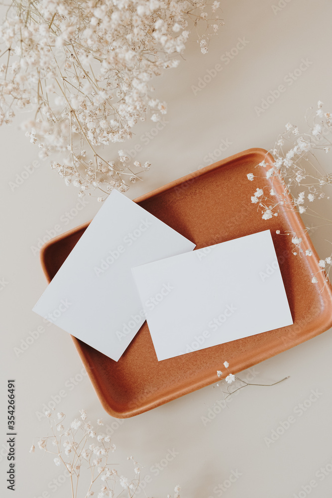 Blank paper cards with mockup copy space on plate and gypsophila flowers on beige background. Minimal business brand template. Flat lay, top view. - obrazy, fototapety, plakaty 