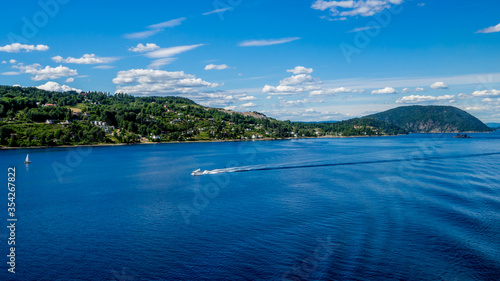 panorama of the oslofjord with two white boats in front of green hills with houses nearby saetre, norway