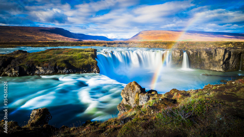 dynamic longtime exposure wide angle panorama of magical godafoss waterfall with romantic rainbow and hills in the background nearby fossholl in iceland