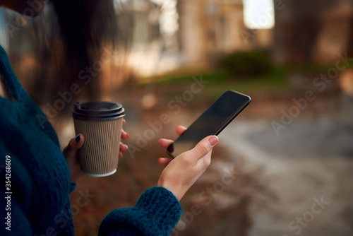 Unknown female holding paper glass of coffee and mobile phone on a hike
