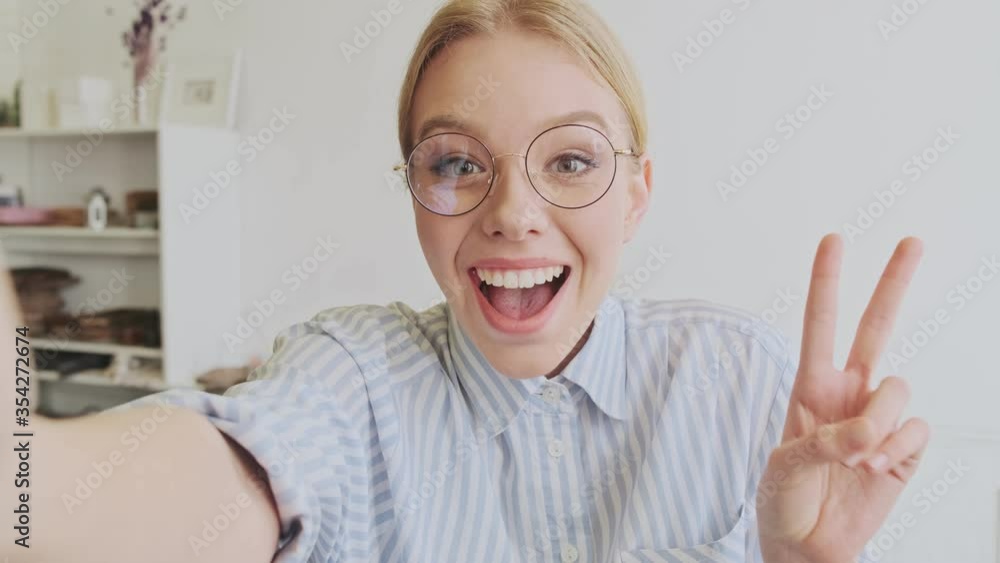 A cheerful young blonde woman architect wearing glasses is taking selfie-photo in the modern office A cheerful young blonde woman architect wearing glasses is taking selfie-photo in the modern office