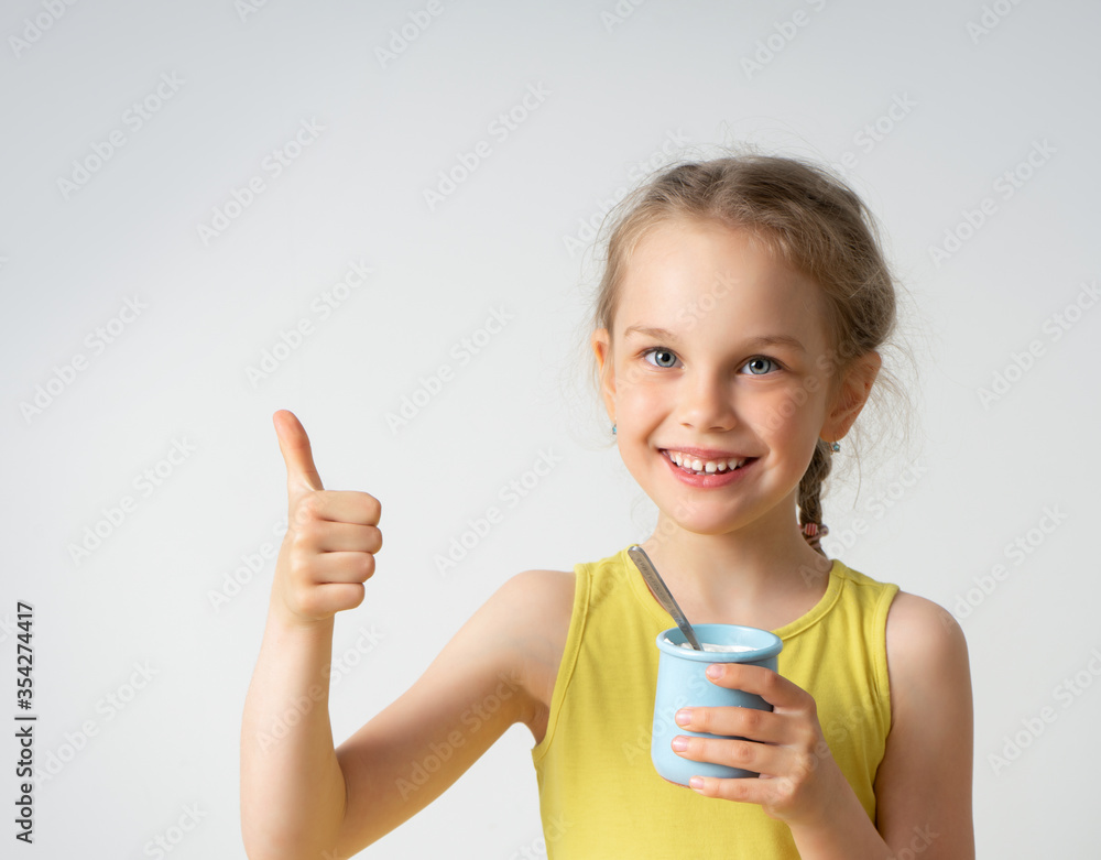 Adorable smiling little girl with a delicious dessert in hand looking at camera showing thumb up. Facial expression, children, summer time, healthy food. Close up studio portrait isolated on white Adorable smiling little girl with a delicious dessert in hand looking at camera showing thumb up. Facial expression, children, summer time, healthy food. Close up studio portrait isolated on white