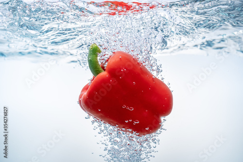 Falling red bell peppers in ecological clear water. Close-up.