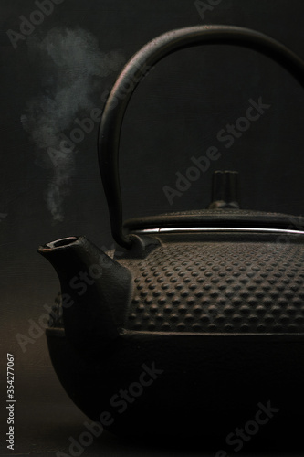 a single black Japanese tetsubin tea pot with steam coming from spout, shot portrait orientation against a black background