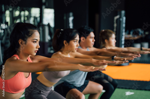 Close-up of group of athletic young Asian people in sportswear doing squat and exercising at the gym. Intense workout and healthy lifestyle concept