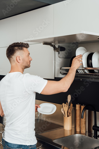 handsome man putting clean plates in plate dryer