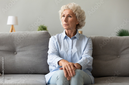Pensive elderly woman sitting on couch looking away lost deep in her thoughts, she looks worried concerned or lonely, female has senile diseases symptoms memory loss, dementia, mental disorder concept © fizkes