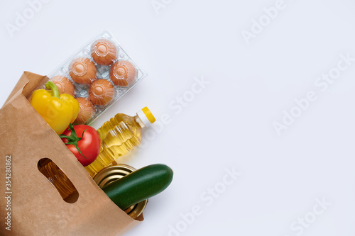 Fototapeta Naklejka Na Ścianę i Meble -  Red tomatoes, zucchini, yellow pepper, chicken eggs, canned food, sunflower oil in paper bag. Fresh vegetables in the bag, top view flatlay photo on white background. The concept of healthy diet