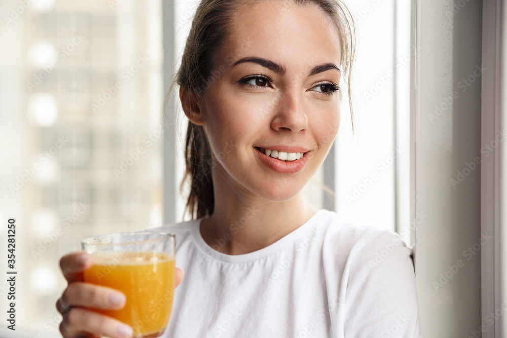 Image of pleased woman smiling and drinking fresh juice while standing Image of pleased woman smiling and drinking fresh juice while standing
