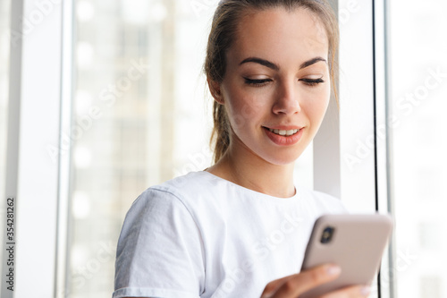 Image of cheerful woman using cellphone and smiling while standing