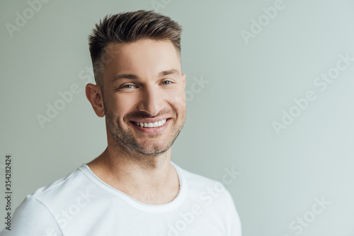 Handsome man smiling while looking at camera isolated on grey