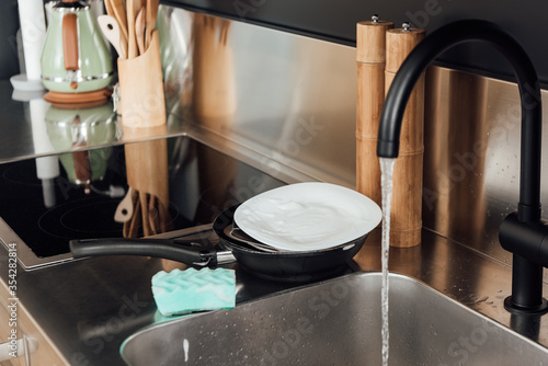 Selective focus of plate  frying pan and sponge in soap near kitchen sink with faucet