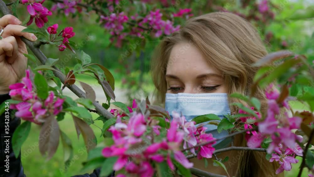 Beautiful girl in a mask sniffs cherry flowers Beautiful girl in a mask sniffs cherry flowers