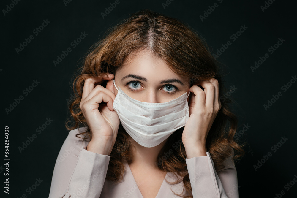 Beautiful young woman wears a respiratory mask, a beautiful female face looks at the camera, a pandemic, a woman's face on a black background, hands in the frame Beautiful young woman wears a respiratory mask, a beautiful female face looks at the camera, a pandemic, a woman's face on a black background, hands in the frame