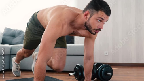 Young man exercising at home. Persistant guy stand in plank position on yoga mat and start doing mountain climber exercise. Moving legs fast and with tempo. photo