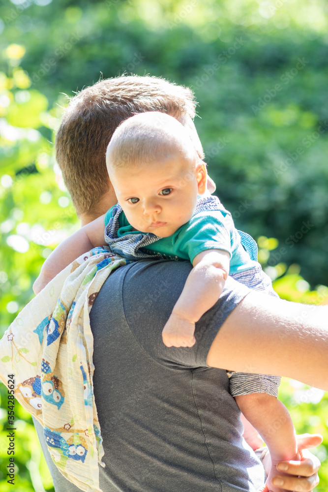 Cute little baby boy spending weekend time with his dad outside. Baby burps on father's shoulder in green park scenery - vacation summer time with baby.