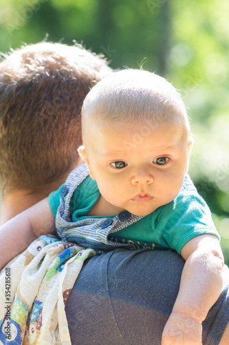 Cute little baby boy spending weekend time with his dad outside. Baby burps on father's shoulder in green park scenery - vacation summer time with baby.