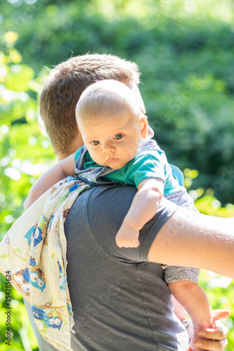 Obraz na płótnie Cute little baby boy spending weekend time with his dad outside. Baby burps on father's shoulder in green park scenery - vacation summer time with baby. w salonie