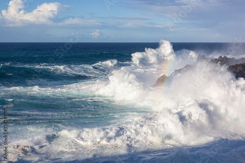 Large surf wave with rainbow in spray is crashing over a volcanic shore on Tenerife island, Canary Islands, Spain
