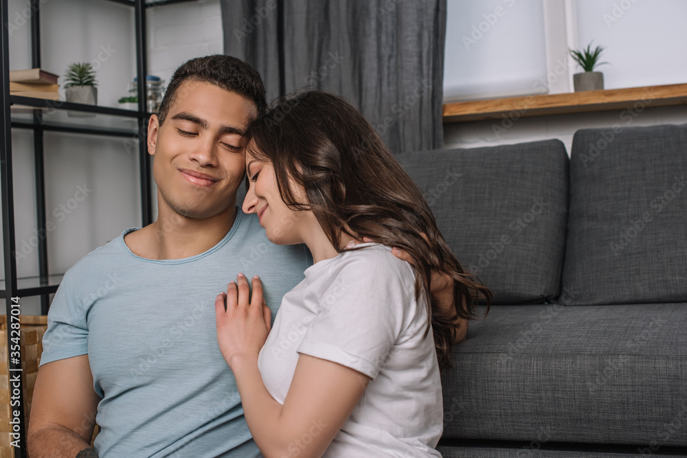 cheerful woman hugging happy mixed race boyfriend at home cheerful woman hugging happy mixed race boyfriend at home