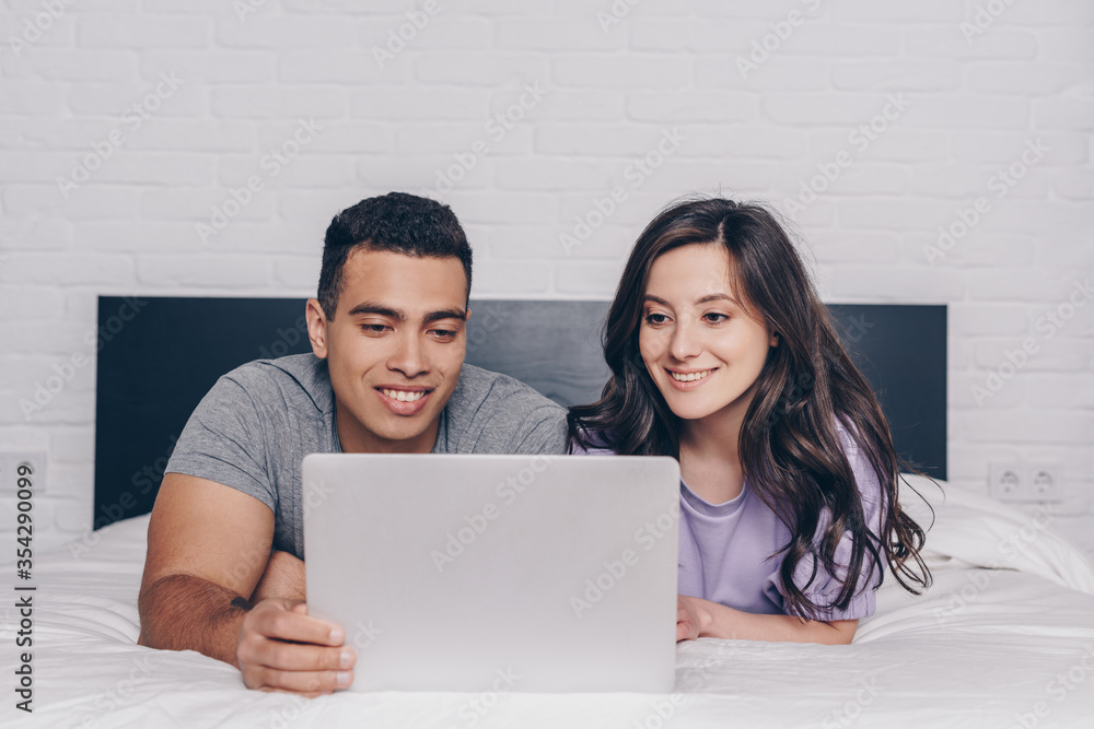 bi-racial man and attractive woman networking while using laptop in bedroom bi-racial man and attractive woman networking while using laptop in bedroom