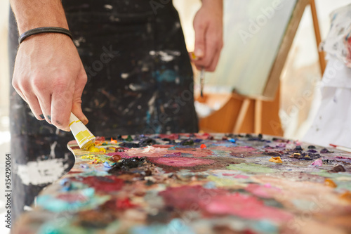 Close up background image of unrecognizable male artist putting paint on palette while painting pictures in art studio, copy space