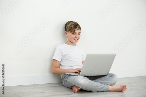 Smiling boy chatting with friends in social networks sitting front laptop .Online study, education .Young boy learning at home during quarantine