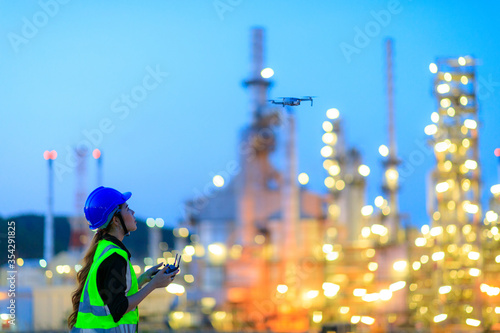 The female engineer using drone for top view inspection the refinery plant.
