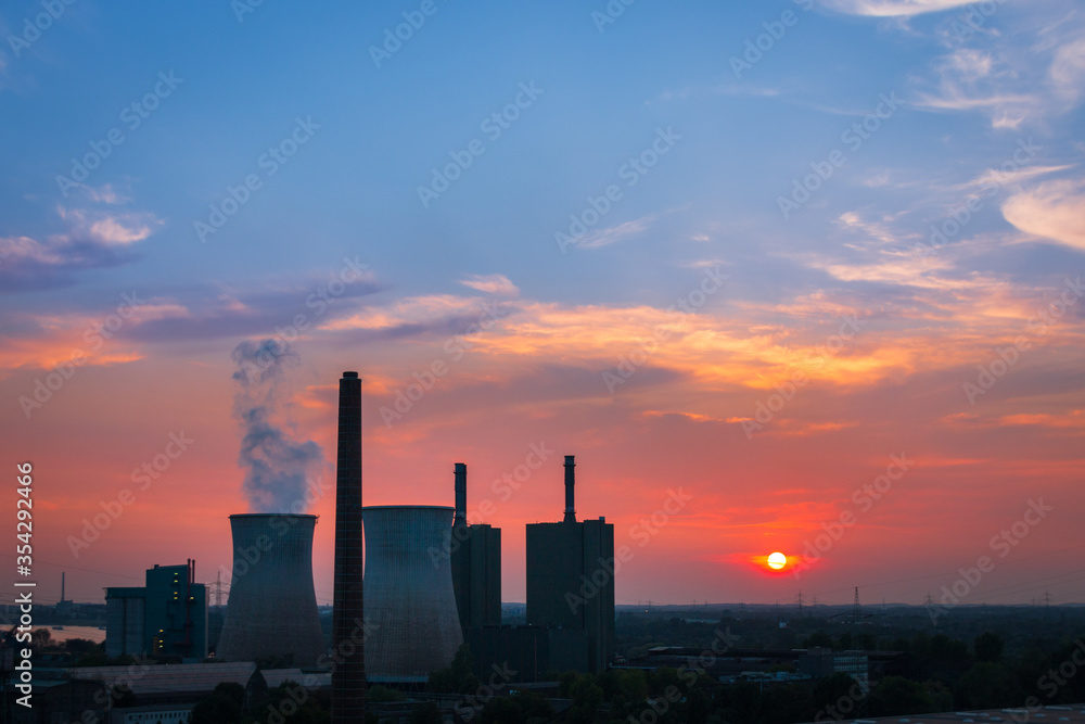 Scenic view of power station and cooling tower at sunset against burning sky.