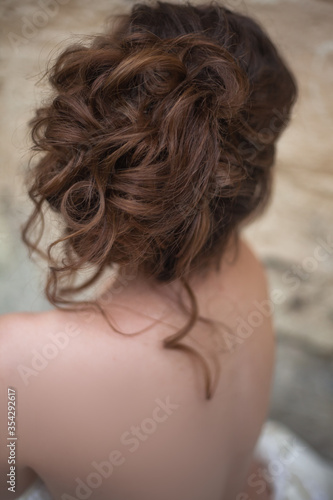 Close-up of back view of woman dressed wedding white dress, make up and hairstyle posing at the background wall at the morning.