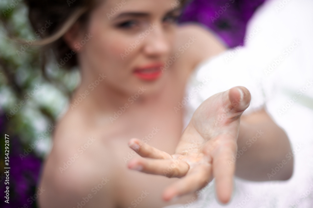 Naklejka premium Close-up of the hand of pretty bride dressed wedding white dress, make up and hairstyle posing at the background flowers wall at the morning with wind in hair.