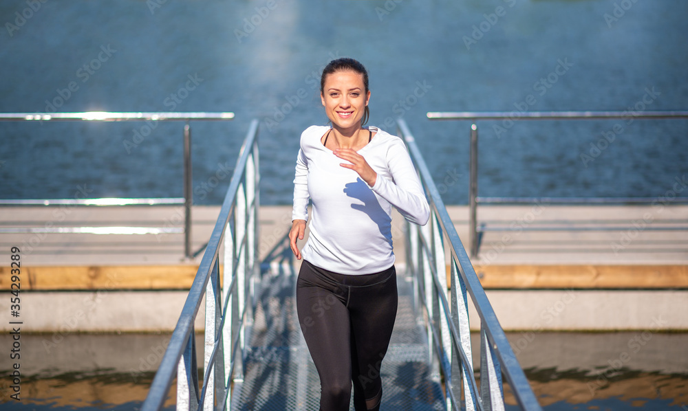 Smiling active young woman running off the walking plank by the river