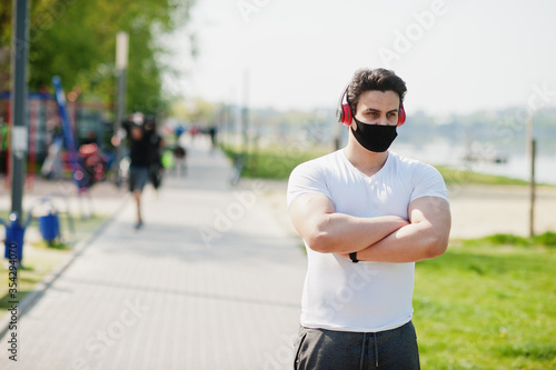 Portrait sports arabian man in black medical face mask posed outdoor with earphones during coronavirus quarantine. © AS Photo Family