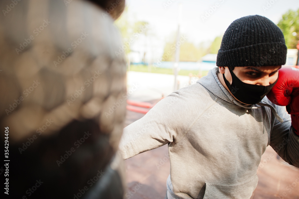 Fototapeta premium Portrait sports arabian boxer man in black medical face mask boxing outdoor during coronavirus quarantine.