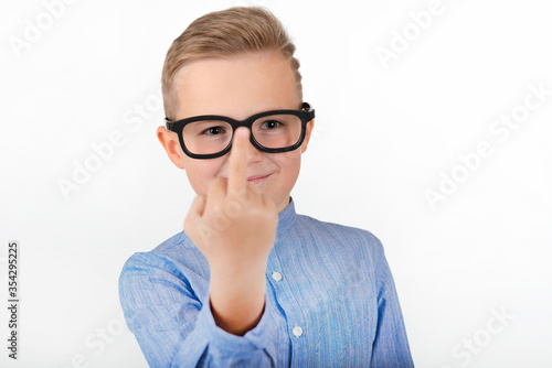 Fototapeta Naklejka Na Ścianę i Meble -  Attractive young caucasian schoolboy with glasses an blue shirt shows middle finger.Close up concept.Studio white wall.