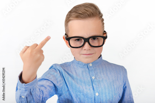 Attractive young caucasian schoolboy with glasses an blue shirt shows middle finger.Close up concept.Studio white wall.