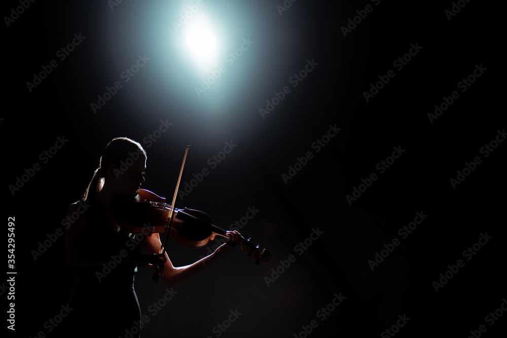 Fototapeta premium silhouette of female musician playing on violin on dark stage with back light