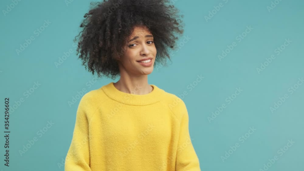 A serious young african american woman with curly hair is refusing of something saying NO isolated over blue wall background in studio A serious young african american woman with curly hair is refusing of something saying NO isolated over blue wall background in studio