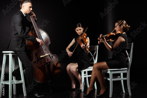 trio of professional musicians playing on musical instruments on dark stage photo