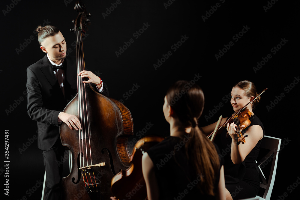 Fototapeta premium trio of musicians playing on double bass and violins isolated on black