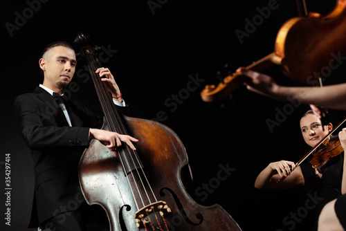 professional musicians playing on double bass and violins isolated on black