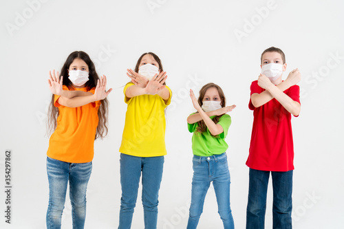 Group of schoolchildren children in colorful T-shirts and medical masks showing crossed hands gesture while looking at the camera over white background. Isolated. Say No to the coronavirus