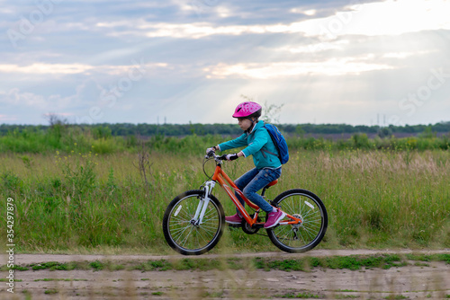 A little girl rides a bicycle on a country road along the meadow.