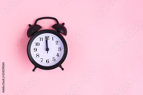 View from above on black alarm clock on pink background. 12 a.m. Time is now