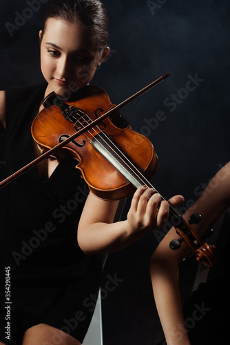 professional beautiful musicians playing classical music on violins on dark stage