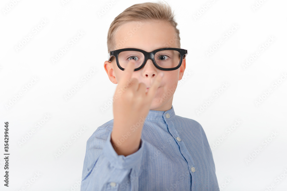 Young Caucasian boy in glasses,blue shirt and shows hands with rock gesture.Studio portrait,white wall.