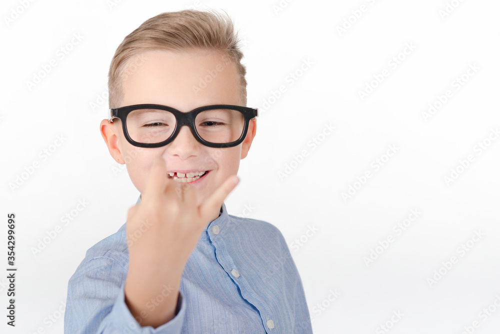 Young Caucasian boy in glasses,blue shirt and shows hands with rock gesture.Studio portrait,white wall. Young Caucasian boy in glasses,blue shirt and shows hands with rock gesture.Studio portrait,white wall.