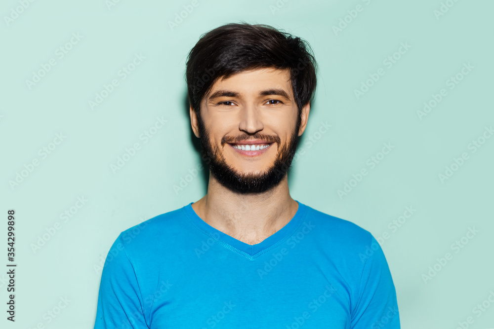 Studio portrait of young smiling guy in blue shirt on background of aqua menthe color.