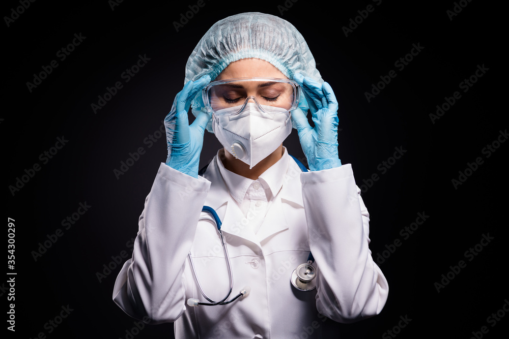 Photo of tired lady doc hold arms on protective plastic goggles undressing after last late operation wear gloves mask coat facial glasses specs surgical cap isolated black color background Photo of tired lady doc hold arms on protective plastic goggles undressing after last late operation wear gloves mask coat facial glasses specs surgical cap isolated black color background