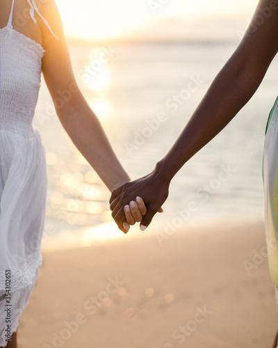 A black woman and a white woman holding hands at the beach. 
